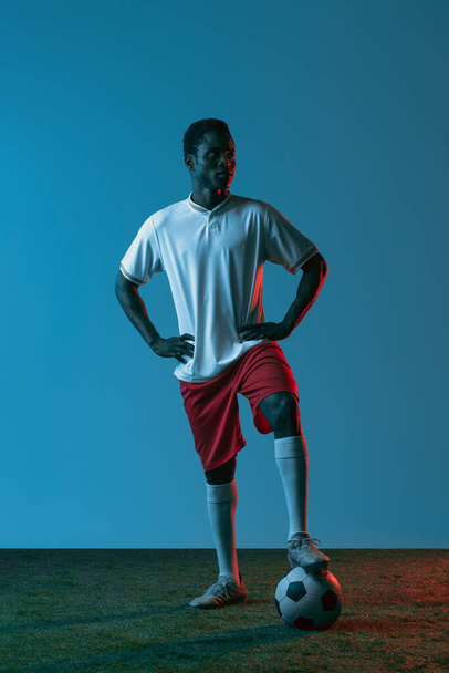 Молодий африканський футболіст, що полює на синьому тлі в неоновому світлі. - Фото, зображення