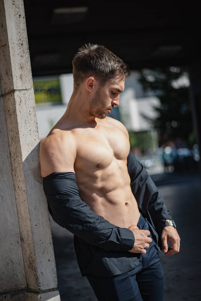 Handsome muscular man in a shirt taken off his shoulders outdoors. Man standing leaning against the wall. Strong sexy athlete. - Foto, imagen