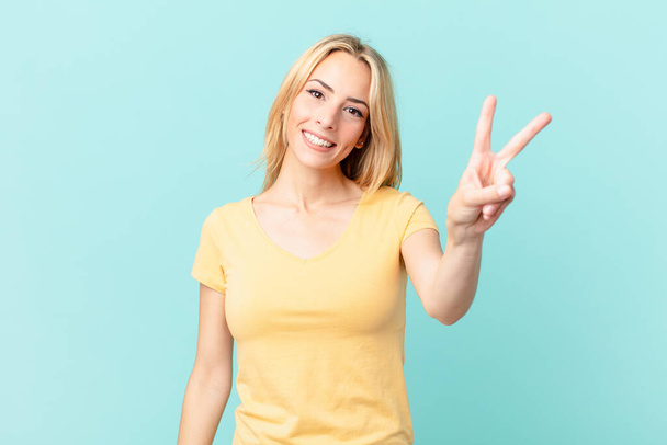 young blonde woman smiling and looking happy, gesturing victory or peace - Φωτογραφία, εικόνα