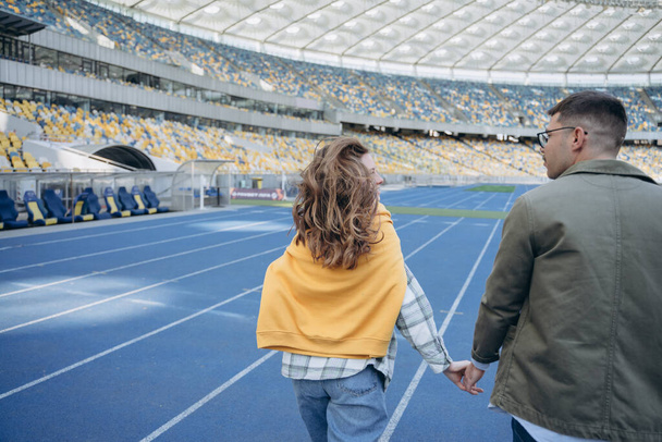 photo of a couple fooling around on empty field stadium, a girl and a guy are holding hands and walking around the stadium - Foto, Imagem