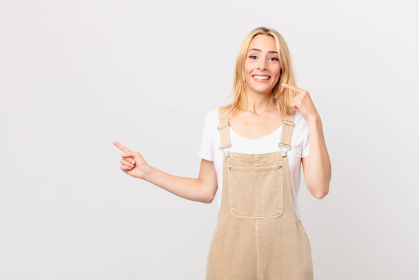 young blonde woman smiling confidently pointing to own broad smile - Фото, изображение