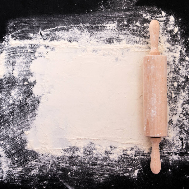 Wooden rolling pin and flour. Bakery on a black stone background. Top view. Free space for text. Background for recipe - Foto, Bild
