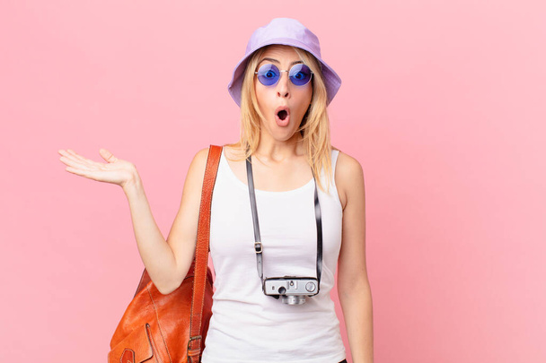 young blonde woman looking surprised and shocked, with jaw dropped holding an object. summer concept - Foto, afbeelding
