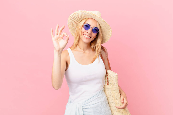 young blonde woman feeling happy, showing approval with okay gesture. summer concept - Foto, Imagen