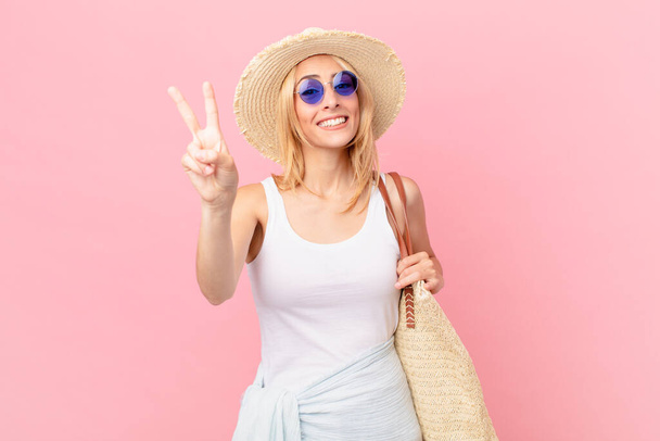 young blonde woman smiling and looking happy, gesturing victory or peace. summer concept - Foto, Bild