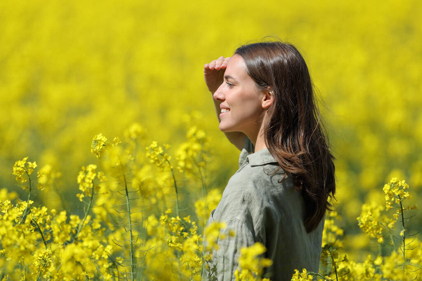 Mujer feliz protegiendo del sol con su mano en un campo de flores amarillas - Foto, Imagen
