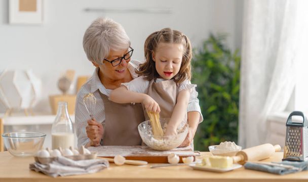 Happy loving family are preparing bakery together. Granny and child are cooking cookies and having fun in the kitchen.  - Foto, afbeelding