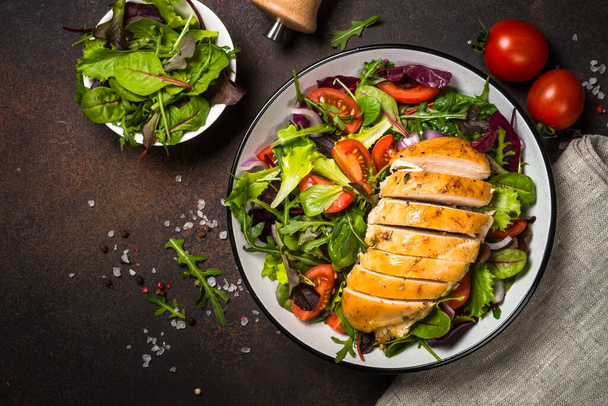 Green salad with baked chicken breast at kitchen table. - Photo, Image