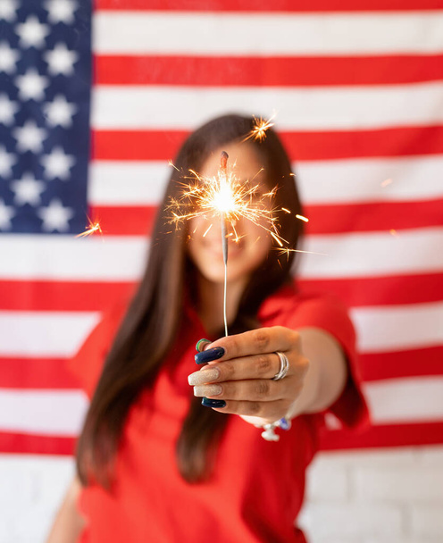 Independence day of the USA. Happy July 4th. Sparkling Bengal fire in caucasian woman hand. Beautiful woman holding a sparkler on US flag background - Valokuva, kuva
