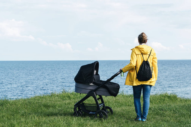 γυναίκα με κίτρινο αδιάβροχο και με παιδικό καροτσάκι δίπλα στη θάλασσα - Φωτογραφία, εικόνα
