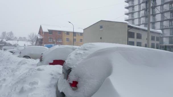 Auto 's bedekt met sneeuw na een sneeuwstorm. Woningbouw op de achtergrond. - Video