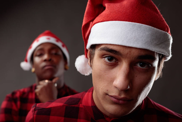 Studio käsite kaksi nuorta miestä juhlii joulua yllään punaiset paidat ja Santa hatut poseeraa toistensa takana samanlaisia harkittuja ilmaisuja ja keskittyä mies etualalla - Valokuva, kuva