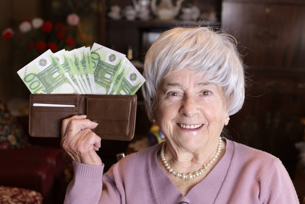 close-up portrait of mature woman holding wallet full of cash at home - Foto, afbeelding