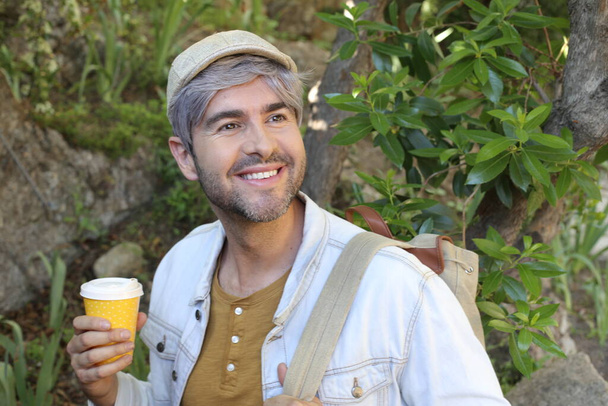 крупным планом портрет красивого взрослого мужчины с седыми волосами, держащего бумажную чашку кофе на природе - Фото, изображение