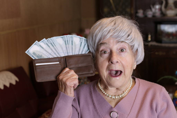 close-up portrait of mature woman holding wallet full of cash at home - Фото, изображение