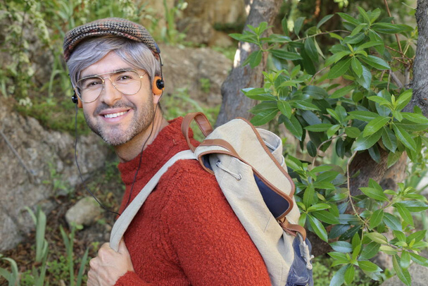 крупным планом портрет красивого взрослого мужчины с седыми волосами в стильной одежде с рюкзаком на природе - Фото, изображение