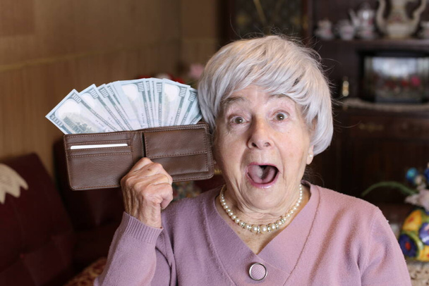close-up portrait of mature woman holding wallet full of cash at home - Foto, Bild