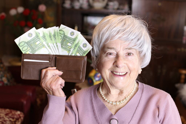 close-up portrait of mature woman holding wallet full of cash at home - Foto, afbeelding