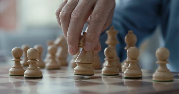 Senior man playing chess, he is moving a piece on the chessboard - Фото, изображение