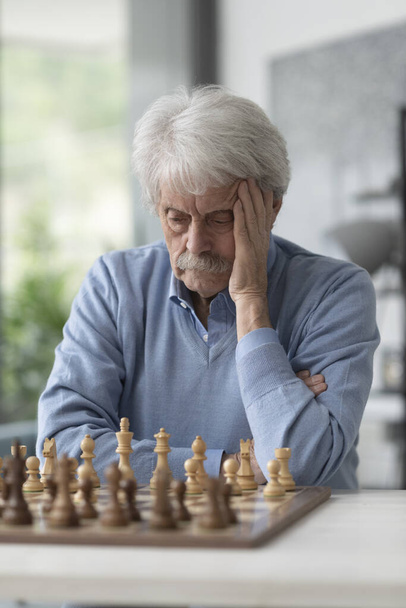 Focused senior man playing chess, he is looking at the chessboard and thinking - Фото, зображення