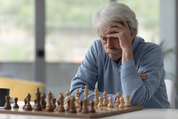 Soustředěný starší muž hraje šachy, dívá se na šachovnici a přemýšlí - Fotografie, Obrázek