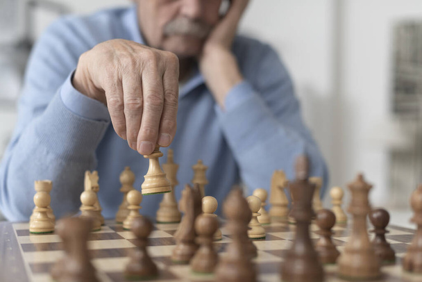 Senior man playing chess and moving a piece on the chessboard - Foto, Imagen