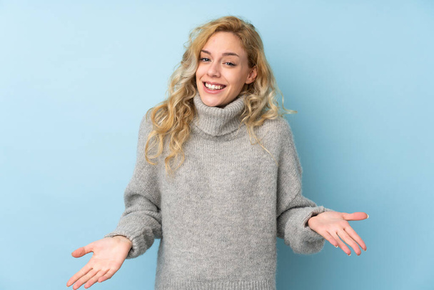 Junge blonde Frau trägt einen Pullover auf blauem Hintergrund und lächelt - Foto, Bild