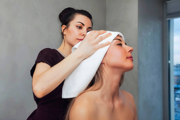 Masseur do makes head massage woman sitting in room on bed with neck and treatment from professional masseuse in SPA salon. Lady getting massaging therapy in SPA resort. Health and beauty concept - Photo, Image