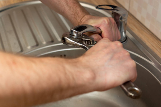 Slotenmaker draai waterkraan in keuken met verstelbare moersleutel bij het repareren - Foto, afbeelding