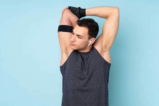 Young sport man over isolated on blue background stretching arm - Φωτογραφία, εικόνα