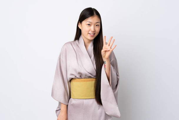 Молодая китаянка в кимоно на изолированном фоне счастлива и считает четверых с пальцами - Фото, изображение