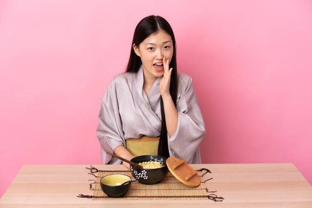 Young Chinese girl wearing kimono and eating noodles shouting with mouth wide open - Photo, Image