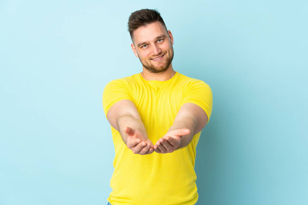 Russian handsome man isolated on blue background holding copyspace imaginary on the palm to insert an ad - Foto, Bild
