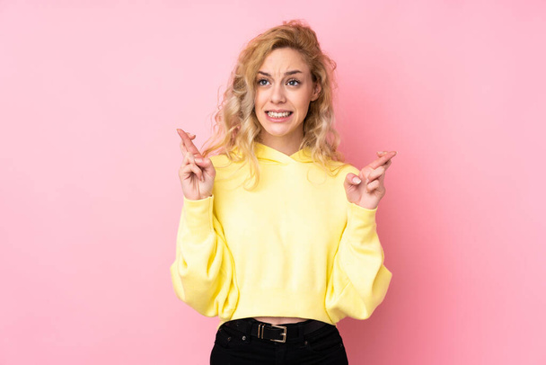 Молода блондинка в сорочці ізольована на рожевому тлі з пальцями, що схрещуються і бажають кращого
 - Фото, зображення