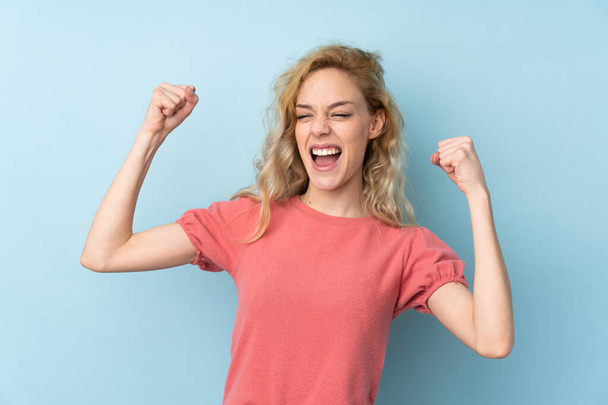 Young blonde woman isolated on blue background celebrating a victory - Photo, Image