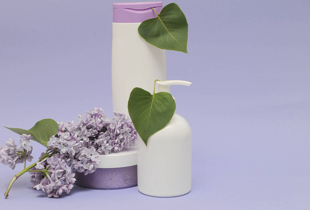 Group of cosmetic bottles with lilac on background.  Face scrub, gel shower and cream on violet background with lilac flowers. - Photo, Image