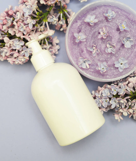 Grupo de garrafas cosméticas com lilás sobre fundo. Esfoliação facial, ducha de gel e creme no fundo violeta com flores lilás. - Foto, Imagem