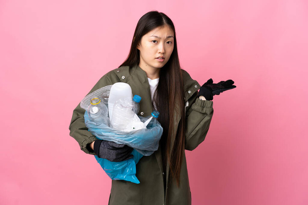 Kiinalainen tyttö tilalla laukku täynnä muovipulloja kierrättää yli eristetty vaaleanpunainen tausta on epäilyksiä - Valokuva, kuva