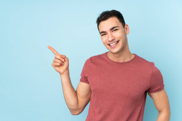 Young caucasian handsome man isolated on blue background pointing finger to the side - Foto, imagen