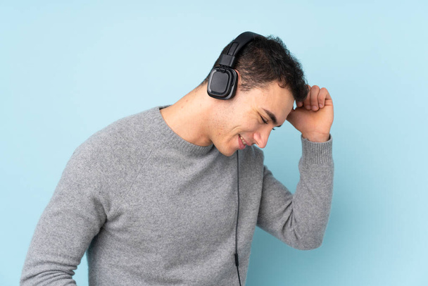 Молодий кавказький красивий чоловік ізольований на синьому фоні слухаючи музику і танці
 - Фото, зображення