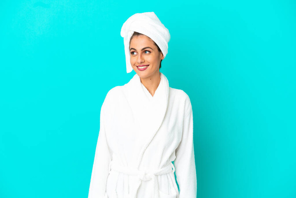 Young woman in a bathrobe over isolated blue background looking to the side and smiling - Foto, Imagen