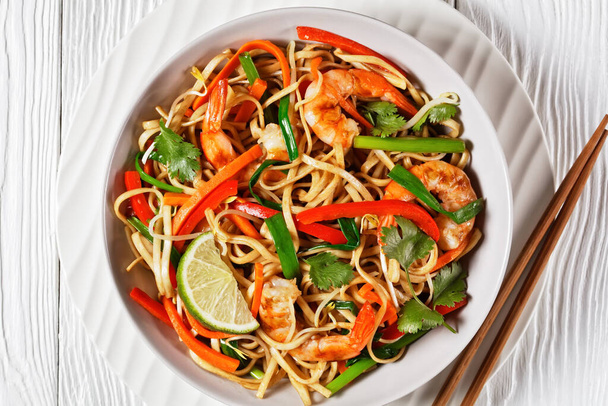 Shrimp Pad Thai with vegetables, tamarind sauce, spring onion and herbs in a white bowl on a wooden table, flat lay,  thai cuisine, close-up - Photo, image