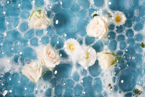 Daisy kwiaty i białe róże w wodzie z pianką. Widok z góry. - Zdjęcie, obraz