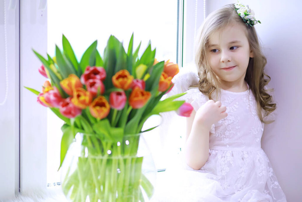 Krásná dívka v bílých šatech s nádhernou kyticí prvních tulipánů. Mezinárodní den žen. Dívka s tulipány. - Fotografie, Obrázek