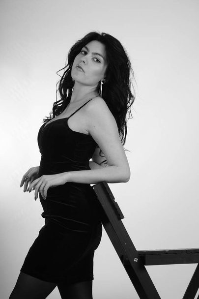 σέξι όμορφη μελαχρινή γυναίκα σε λίγο μαύρο φόρεμα και καλσόν με ψηλά τακούνια ποζάρουν στο στούντιο σε λευκό φόντο  - Φωτογραφία, εικόνα