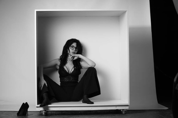 sexy beautiful brunette woman in lingerie and trendy bell bottoms pants posing in decorative box at studio on white background  - Фото, зображення