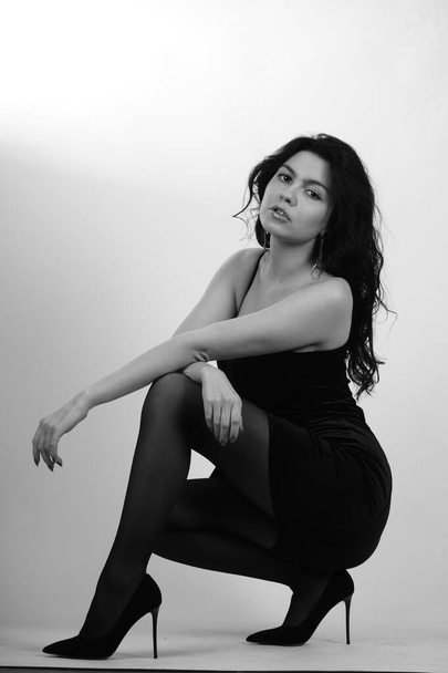 sexy beautiful brunette woman in little black dress and tights with high heels posing at studio on white background  - Φωτογραφία, εικόνα
