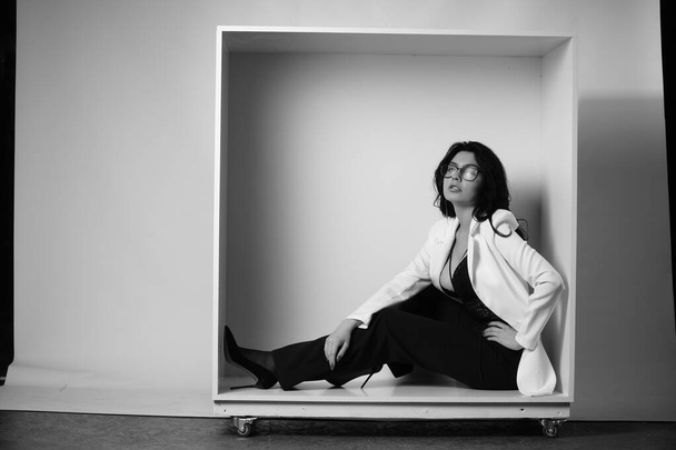 сексуальная красивая брюнетка женщина в белой рубашке с нижним бельем и модные брюки колокольчика позирует в декоративной коробке в студии на белом фоне  - Фото, изображение
