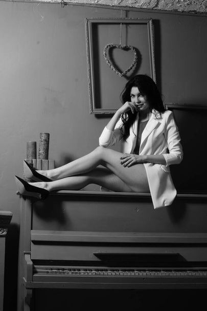 beautiful brunette woman in lingerie and white blazer posing on piano at studio  - Fotoğraf, Görsel