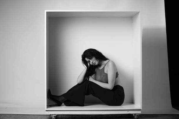 sexy bela morena mulher em lingerie e moderno sino bottoms calças posando em caixa decorativa no estúdio no fundo branco  - Foto, Imagem